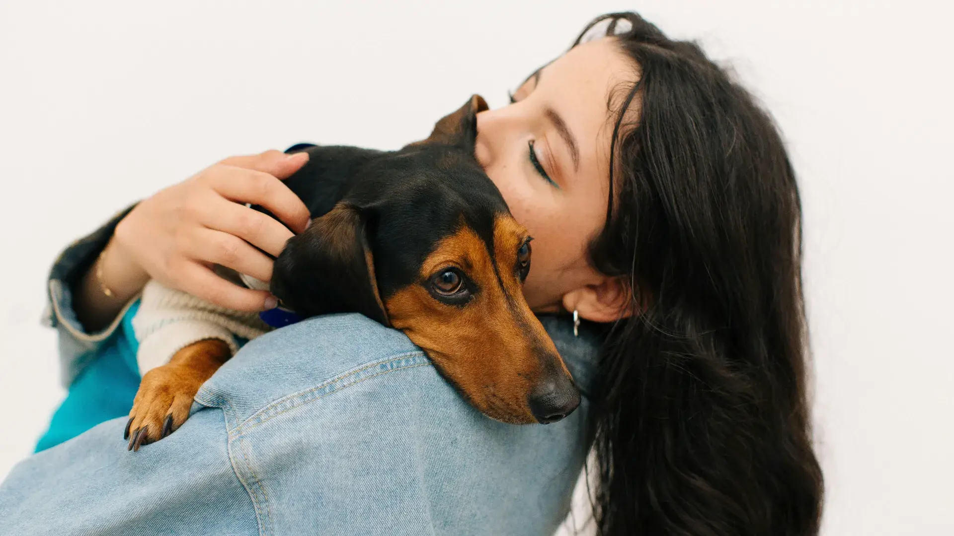 A woman smiling while holding a small black and tan dog close to her face, symbolizing the joy and love that pets bring to their owners' lives.