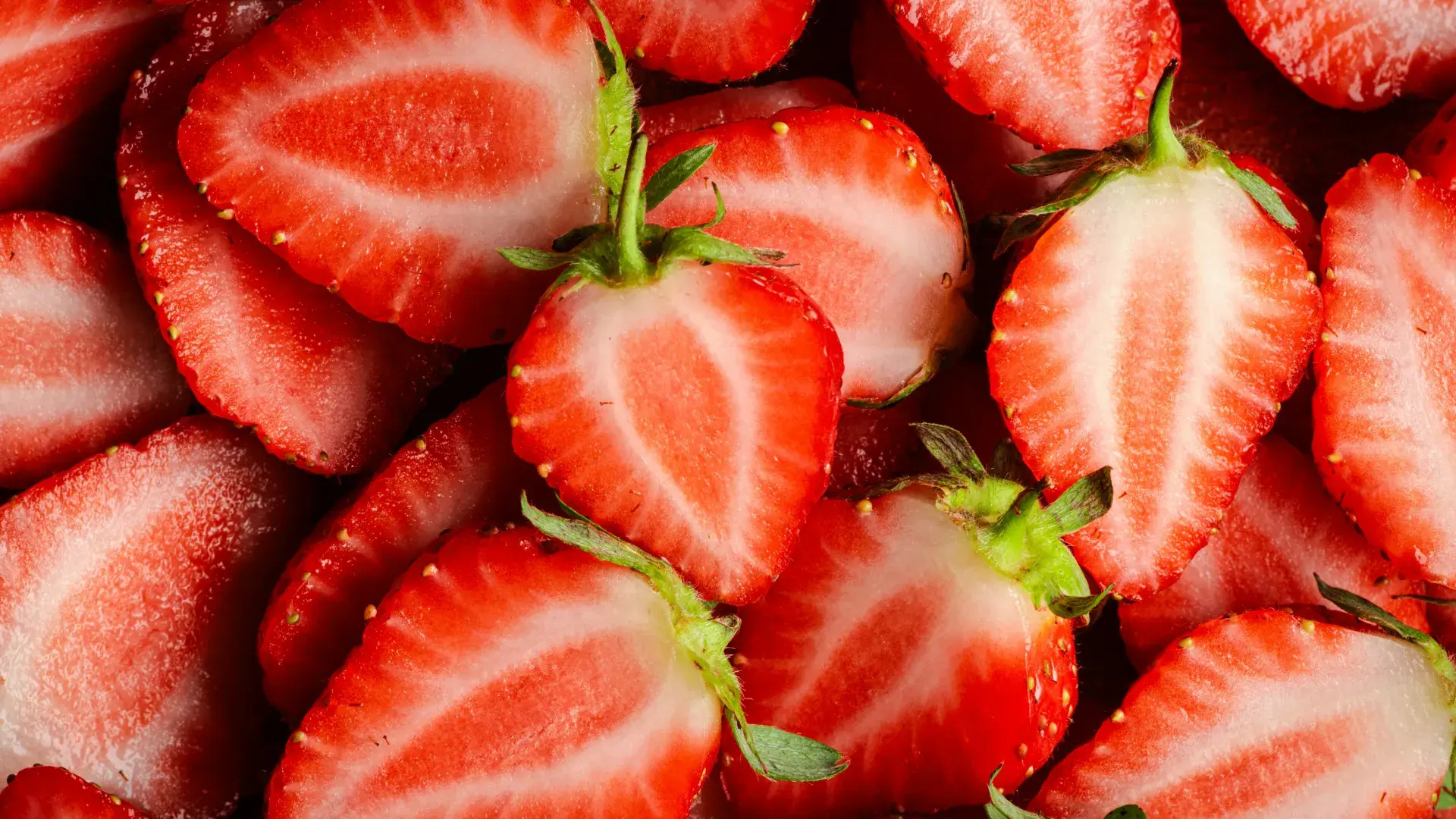 A person hand-feeding a slice of strawberry to a focused dog. The shallow depth of field keeps the dog’s expectant face in sharp focus, illustrating the practice of giving dogs small, manageable fruit pieces.