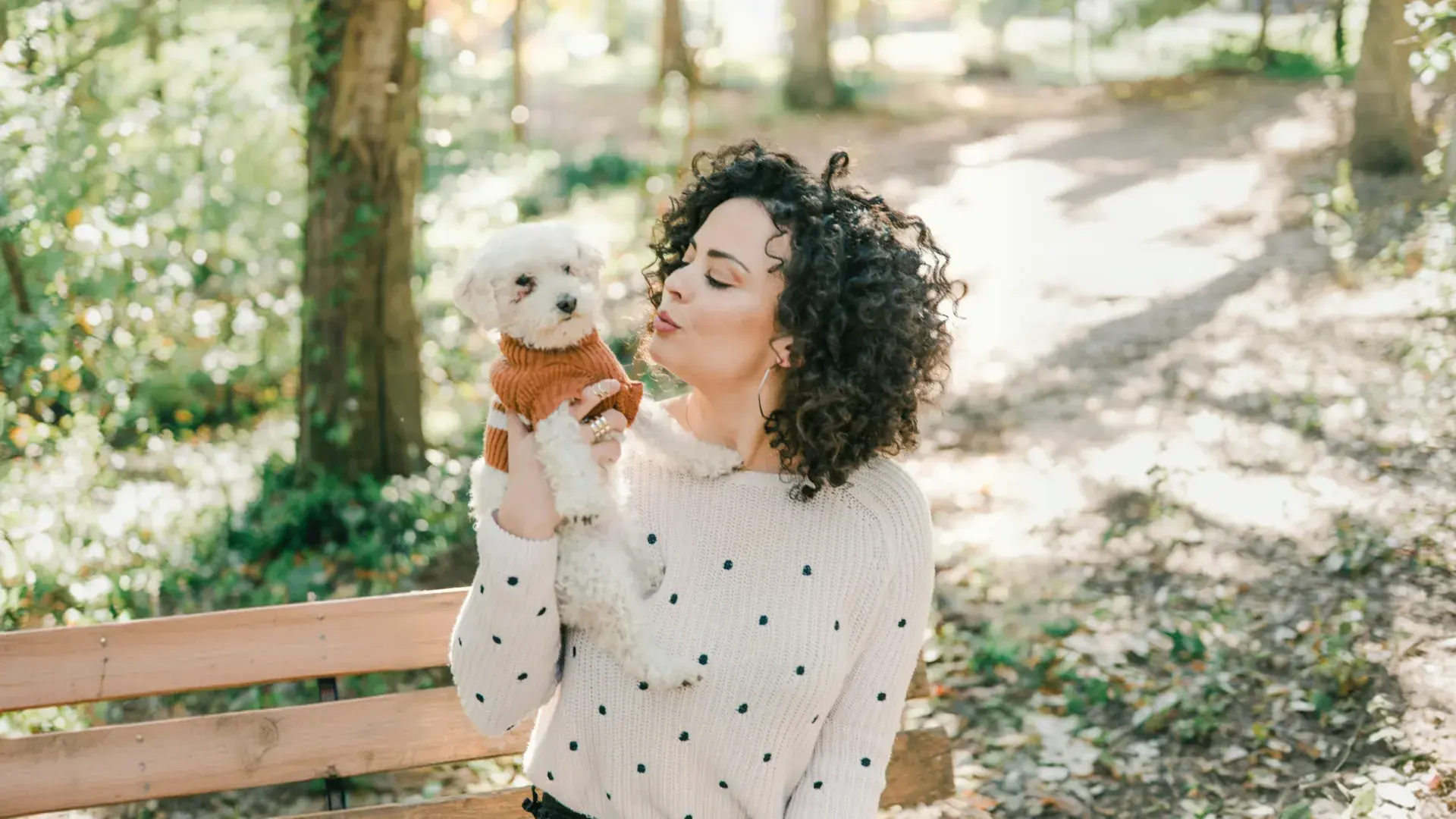 A white dog sitting patiently as its owner leans in for a kiss in a park setting. Understanding if dogs like kisses requires observing their reaction to human affection and physical closeness.